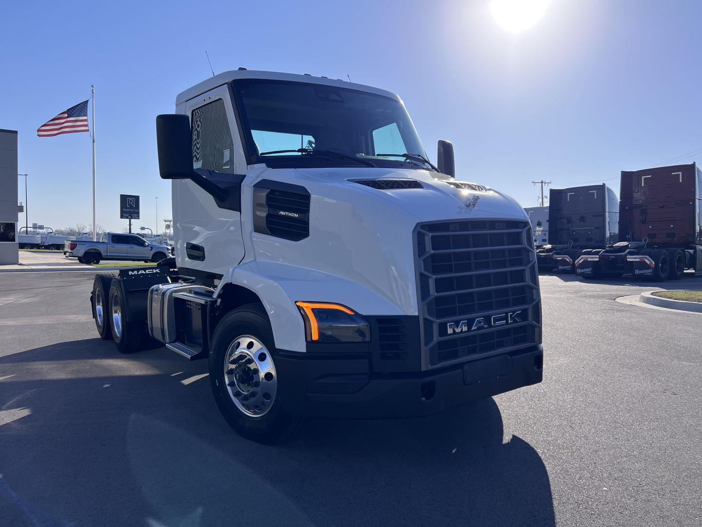 Truck front three-quarter view showing 2027 Mack AN64T Daycab with white cab, black grille, large headlights, and dual rear axles.