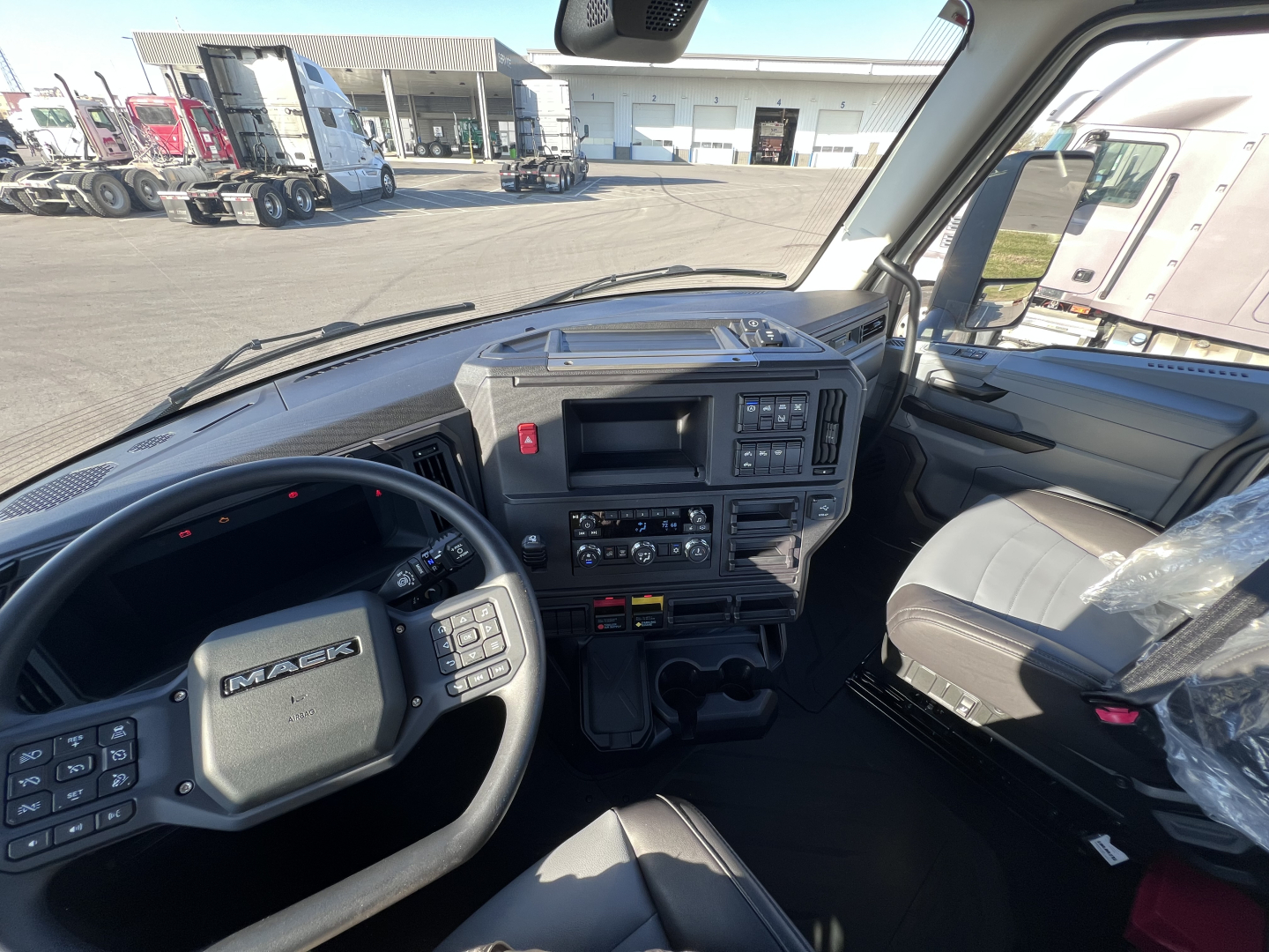 Front interior view of a new 2027 Mack AN64T daycab with steering wheel, dashboard, and driver's seat; visibility shows instrument panel, controls, and center console.