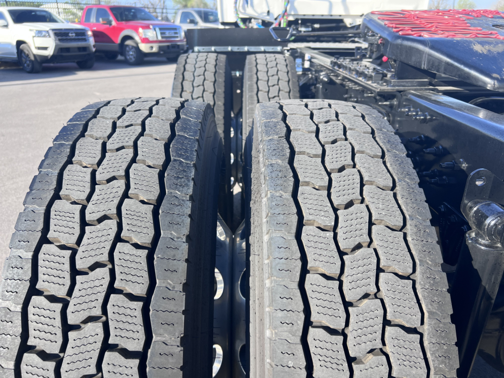 Rear dual tractor tires on a Mack AN64T truck chassis, tread pattern visible with other trucks in background.