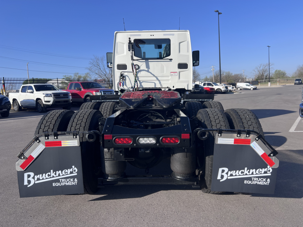 Rear view of a white Mack AN64T truck tractor showing dual rear axles, mud flaps with 'Bruckner's Truck Equipment' logos, and spare tires. Tail lights and hydraulic lines visible.