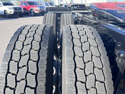 Rear dual tractor tires on a Mack AN64T truck chassis, tread pattern visible with other trucks in background.