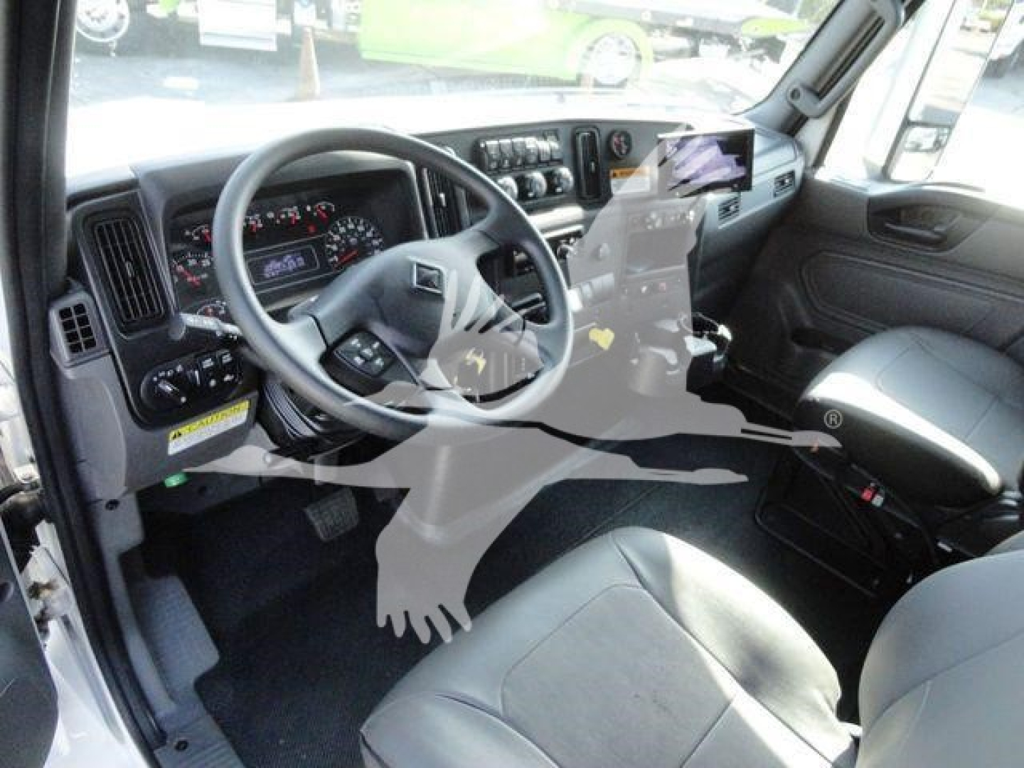 Truck cockpit interior with steering wheel, dashboard gauges, and center console; reflection of dealership lot on windshield.