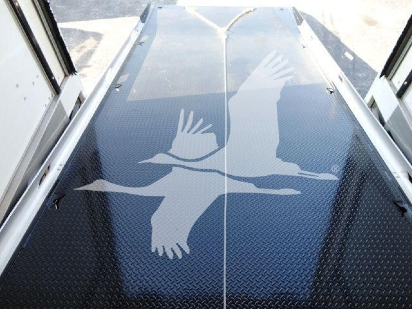 Image of a blue diamond-plate ramp with an overlay of white birds in flight graphic, seen from top-down perspective inside a rollback truck.