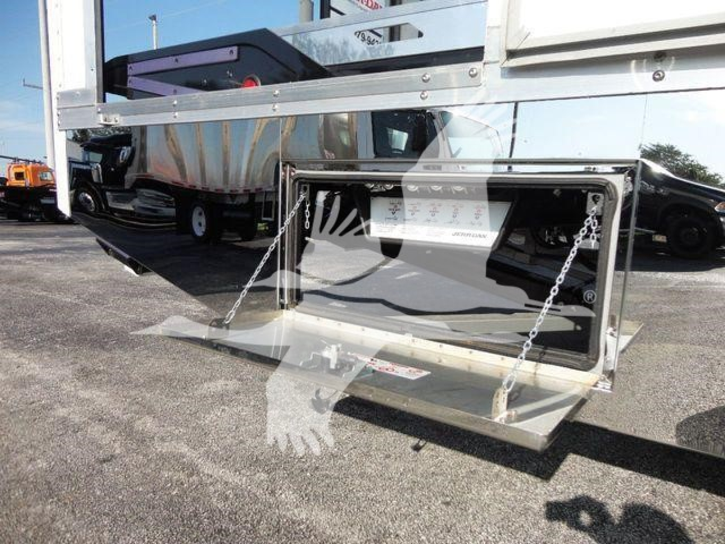 Truck hitch area showing a fold-down platform and chains on the rear of a 2022 International MV rollback truck, with reflective surfaces and cargo bed in the background.