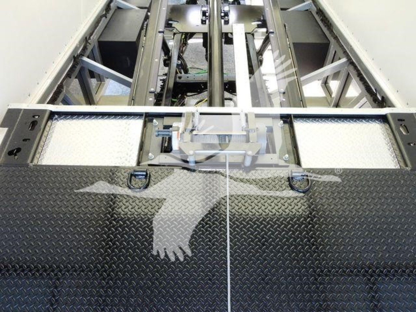 Open-top framework of a rollback truck bed with diamond plate surface and mounting rails, showing structural rails and latch area.