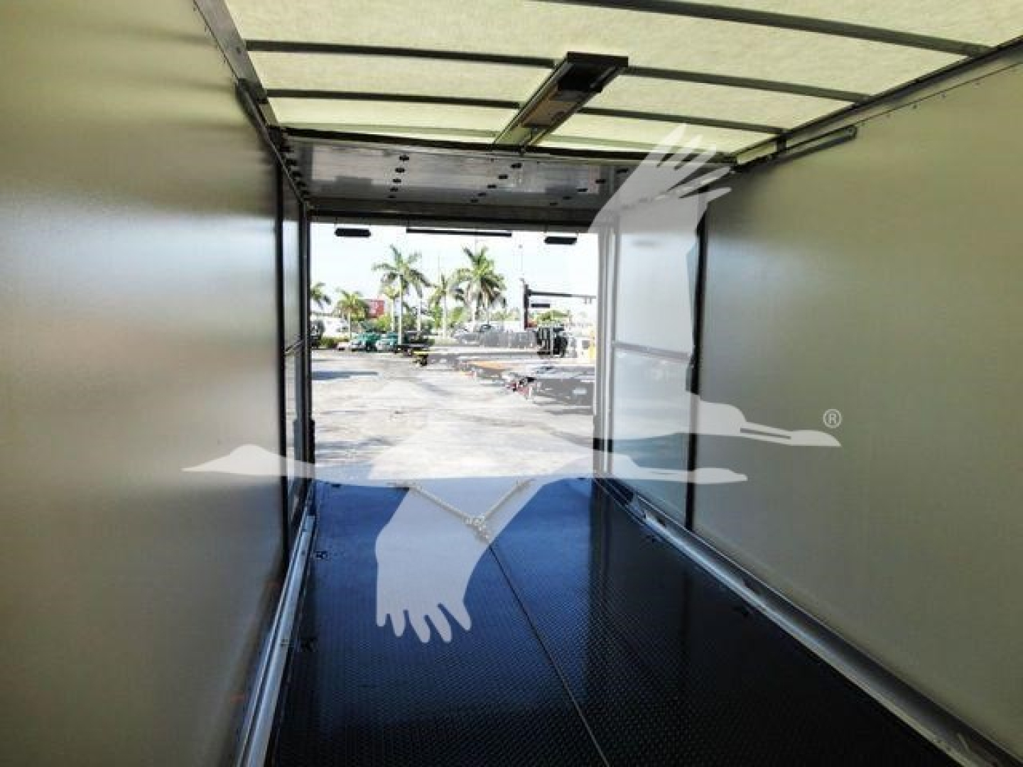 Interior view of a new 2022 International MV rollback truck cargo area, long box with open rear doors showing exterior yard with palm trees and vehicles.