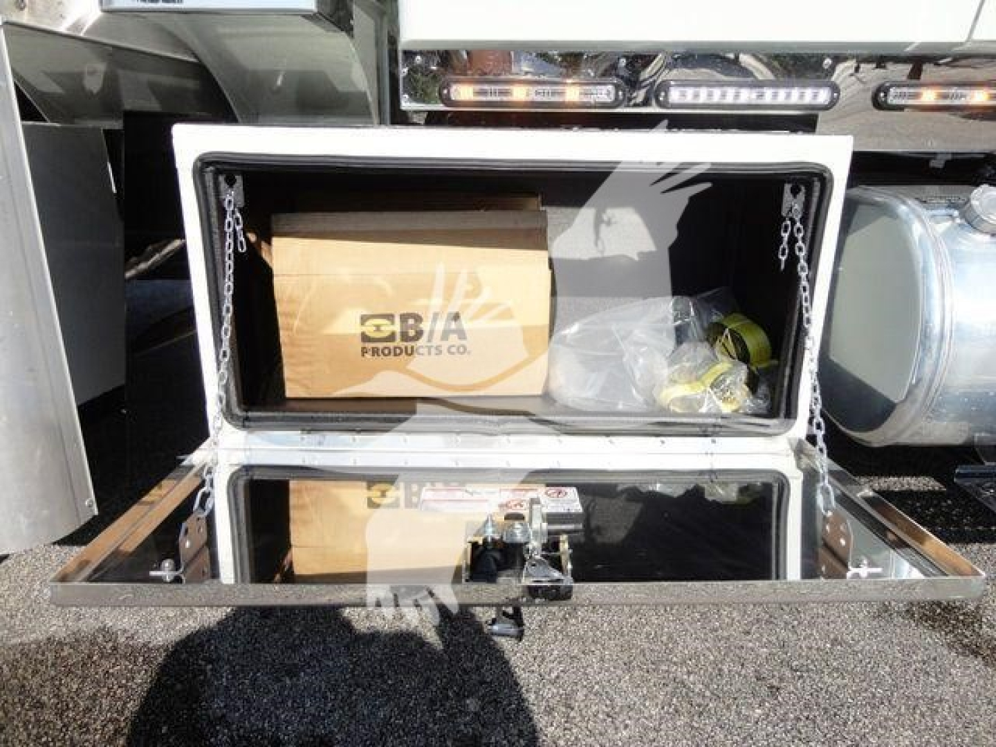 Open storage compartment on an International MV truck showing a box labeled 'SBA PRODUCTS CO.' inside the cooler/compartment with a metal frame and chains.
