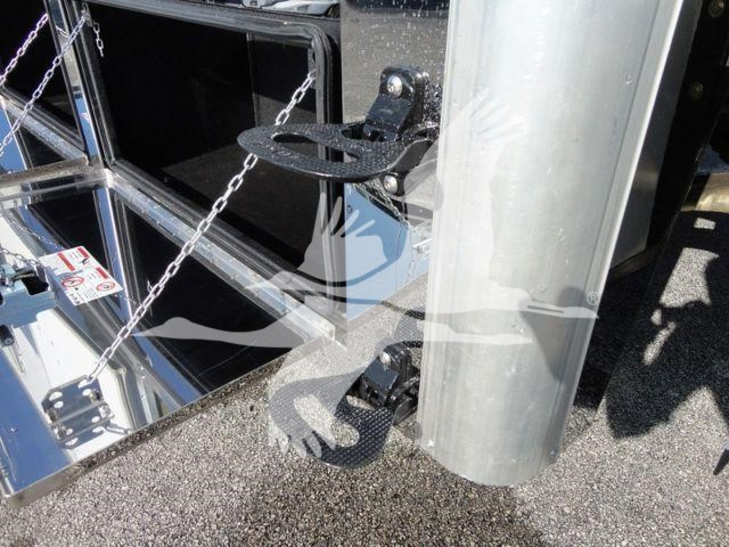 Truck trailer hitch and support leg hardware on a metal trailer with chains and reflective chrome surfaces.