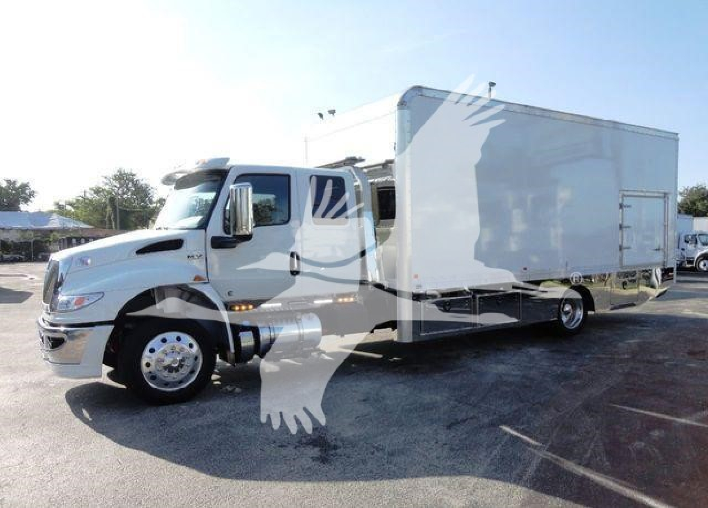 International MV rollback truck with a large white box body, front cab, and dual rear wheels in a dealership lot.