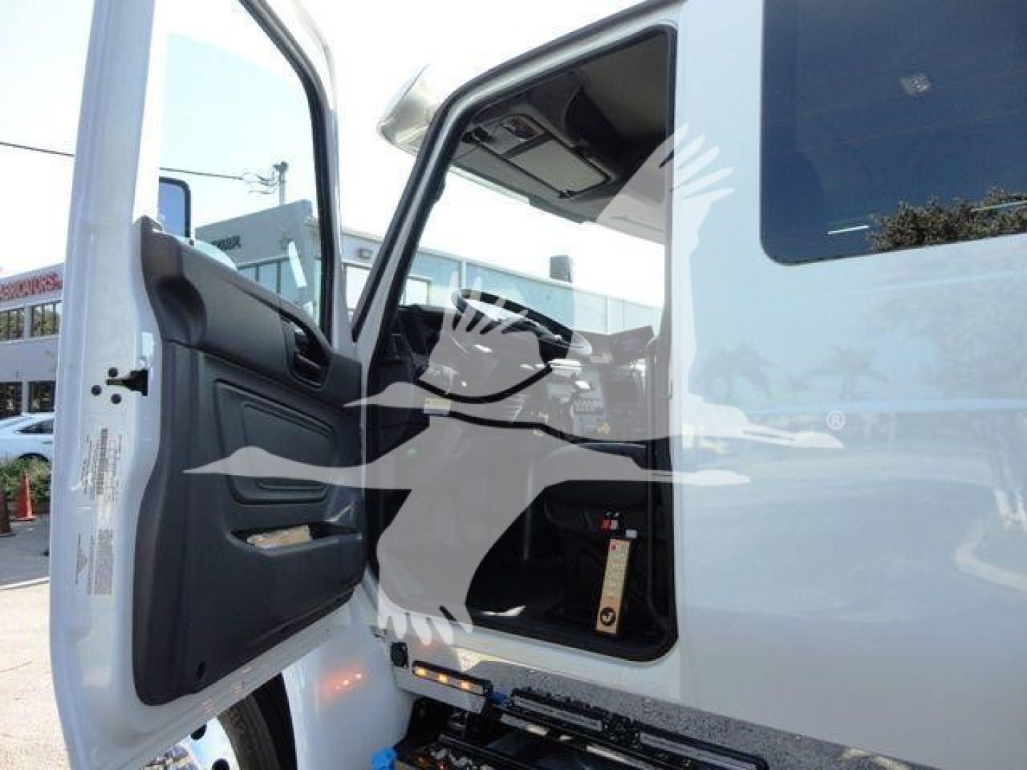 Truck cab interior view with open door showing operator seat area and entry step; some label tags visible near lower dash