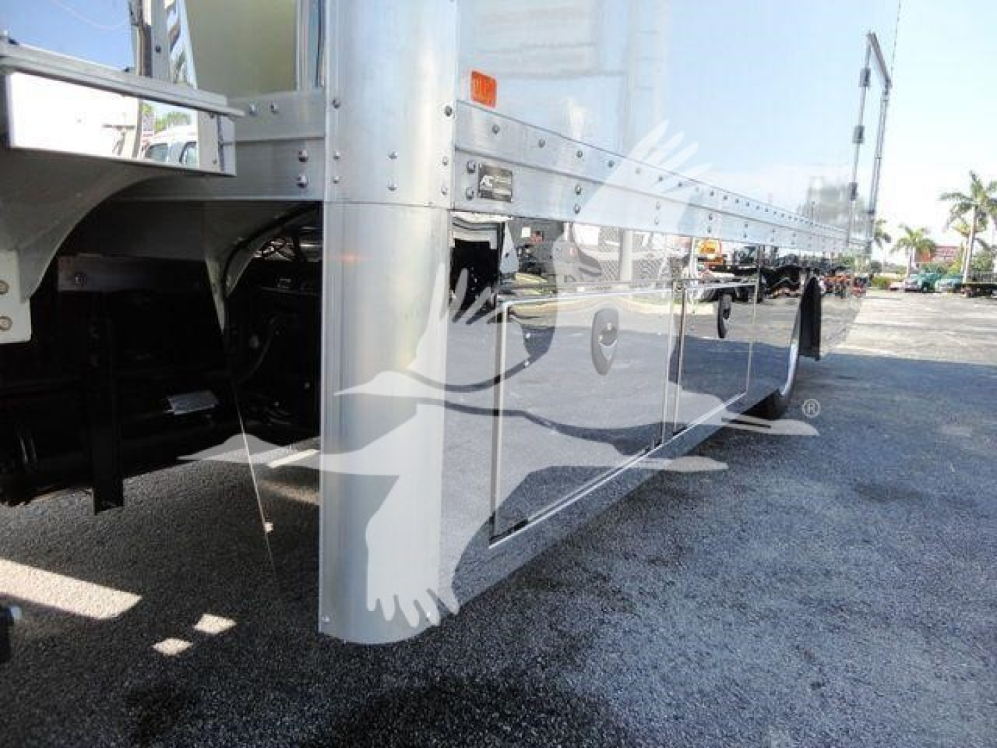 Side view of an aluminum International MV rollback truck showing polished side panels and undercarriage reflection.