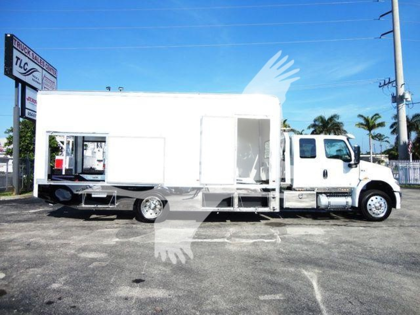 Truck with large white box body and side door, chassis seen in a dealership lot.