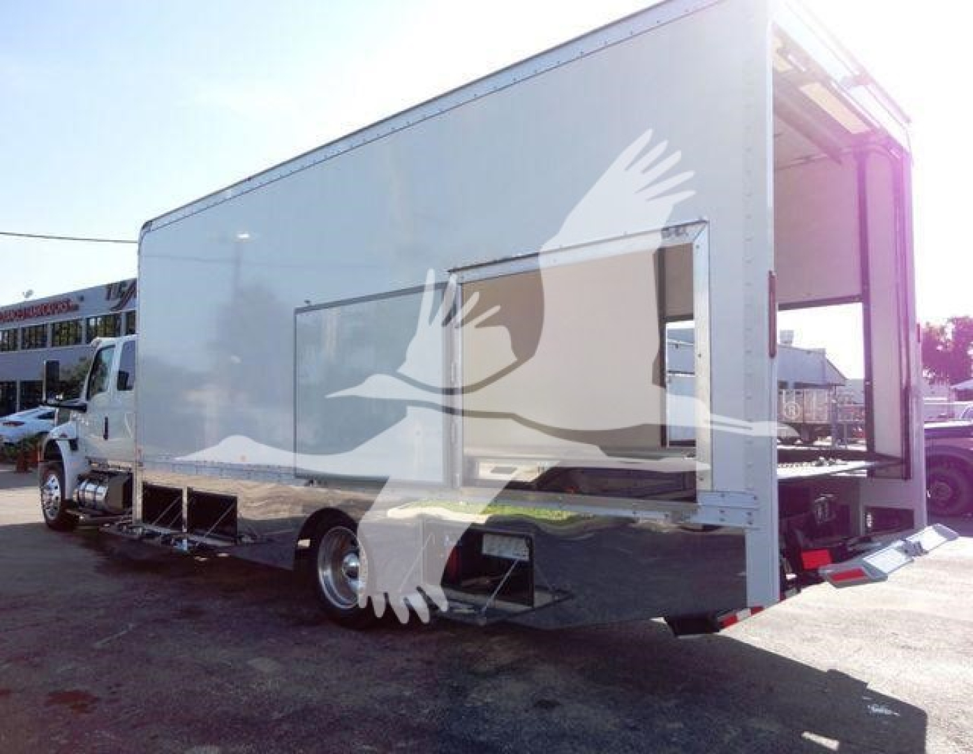Isuzu or similar medium-duty rollback truck with a large rectangular cargo body; side panel with a window/vent and retractable steps; rear platform and tailgate visible.
