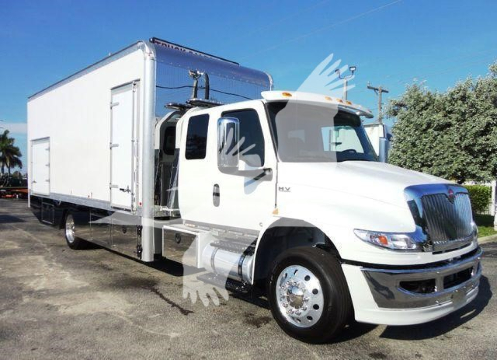 International MV truck in view showing rollback box and cab, white with chrome bumper and large box trailer.