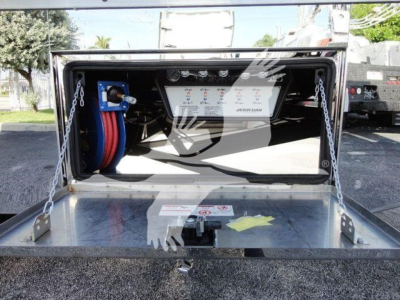 Image showing back end of 2022 International MV rollback truck with service panel, hoses, and control panel inside open storage compartment.