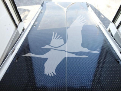Image of a blue diamond-plate ramp with an overlay of white birds in flight graphic, seen from top-down perspective inside a rollback truck.