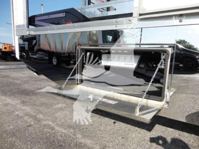 Truck hitch area showing a fold-down platform and chains on the rear of a 2022 International MV rollback truck, with reflective surfaces and cargo bed in the background.