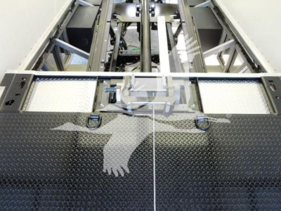 Open-top framework of a rollback truck bed with diamond plate surface and mounting rails, showing structural rails and latch area.