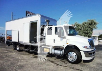 Truck mounted rollback wrecker body on a white International MV cab chassis. Side door open, living quarters module behind cab, logo on front grille visible.
