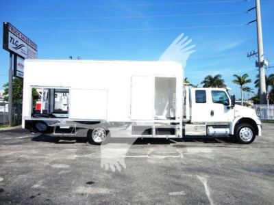 Truck with large white box body and side door, chassis seen in a dealership lot.