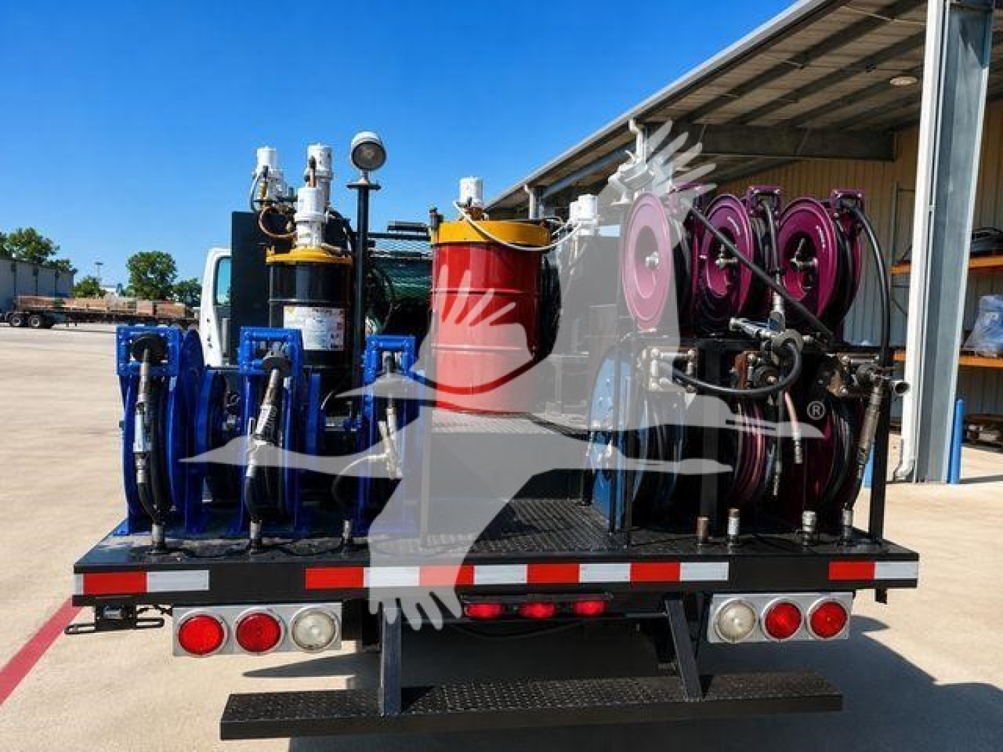 Truck bed showing multiple color-coded hydraulic reels, hoses, and a red container on a 2019 Ford F750 flatbed with rear lights.