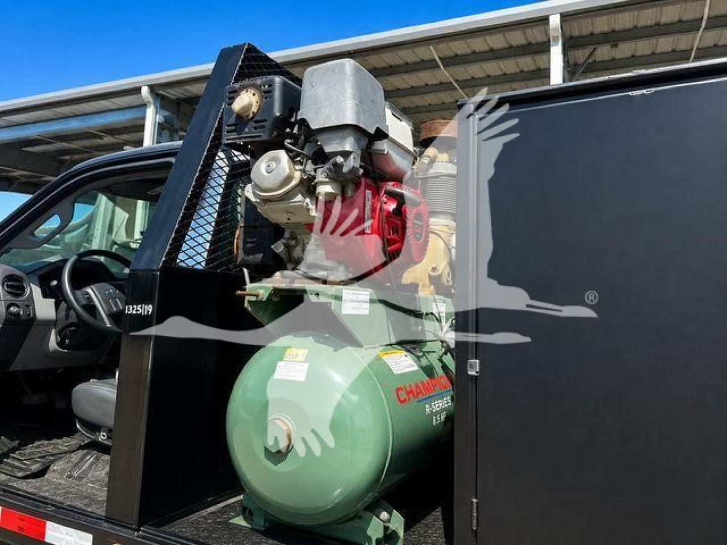Truck cab interior with mounted green propane tank and equipment behind the driver seat; label text visible on circular tank and attached machinery.
