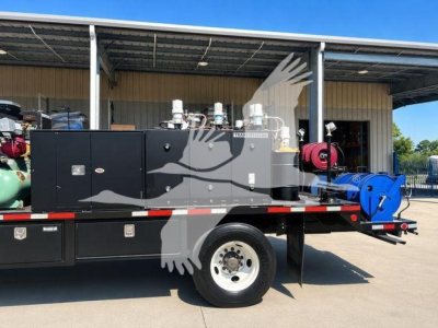 Flatbed tow truck engine bay showing large diesel generator set and control panels on black body with warning labels.