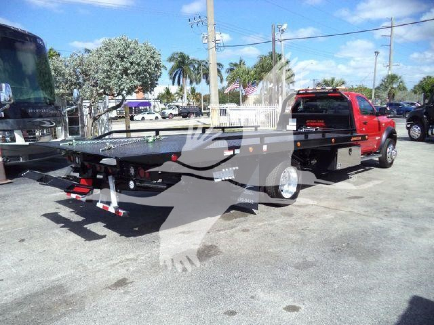 Flatbed rollback truck setup on a 2024 Ram 5500 SLT with dual rear wheels and a black steel flatbed, rear view showing hitch and LED taillights.