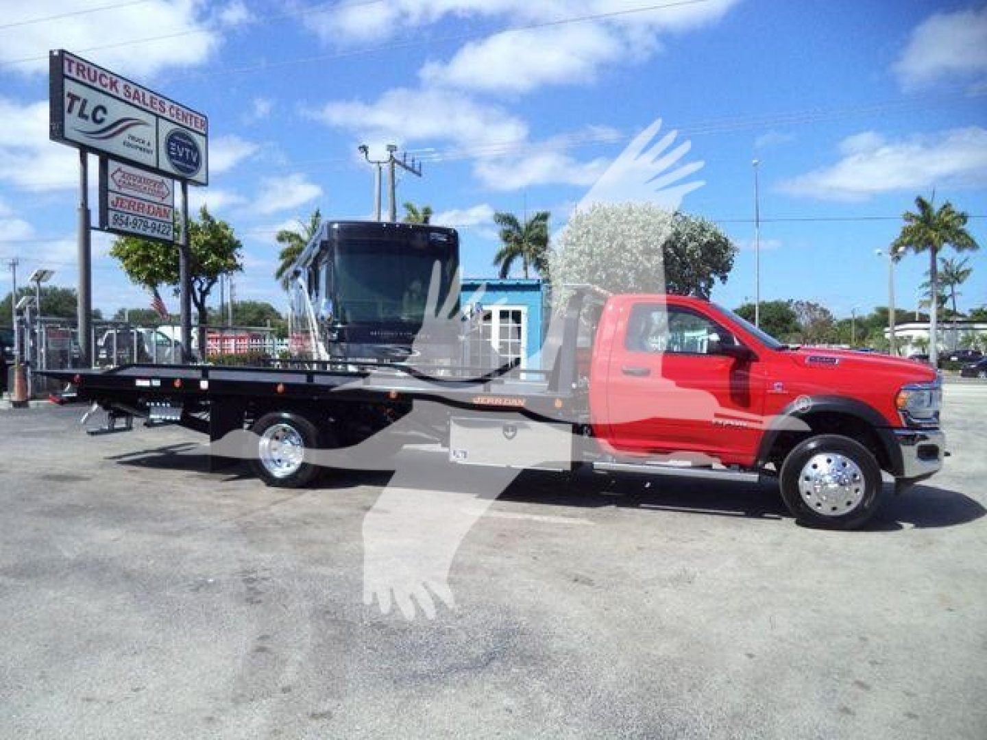 Ram 5500 flatbed tow truck, red cab, long black flatbed, with a tow winch and light bar, side mirror, large wheels, dealership lot in background.