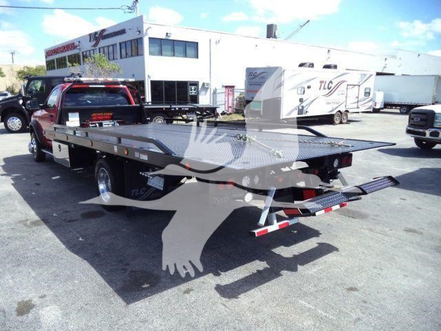Ram 5500 rollback flatbed truck in dealership lot with large flatbed and ramps, red cab, stock number J24798.