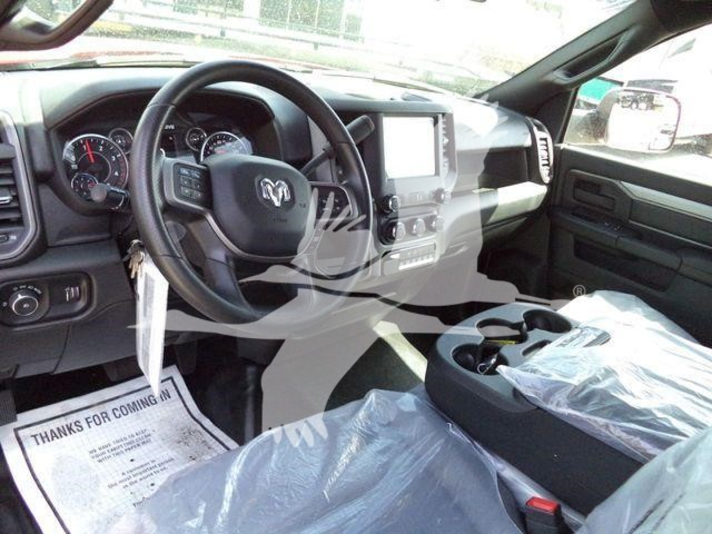 Truck interior showing dashboard, steering wheel with Ram logo, center touchscreen, and wrapped seats in new condition.