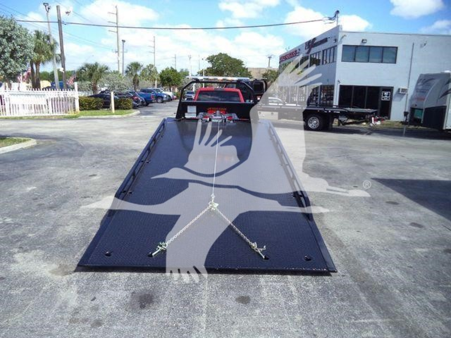 Tow truck with a flatbed ramp open and a white crane silhouette watermark across the image.