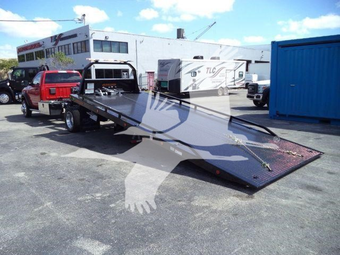 Truck with a flatbed rollback covered by a watermark, showing a red pickup truck towing a flatbed trailer in a dealership lot.