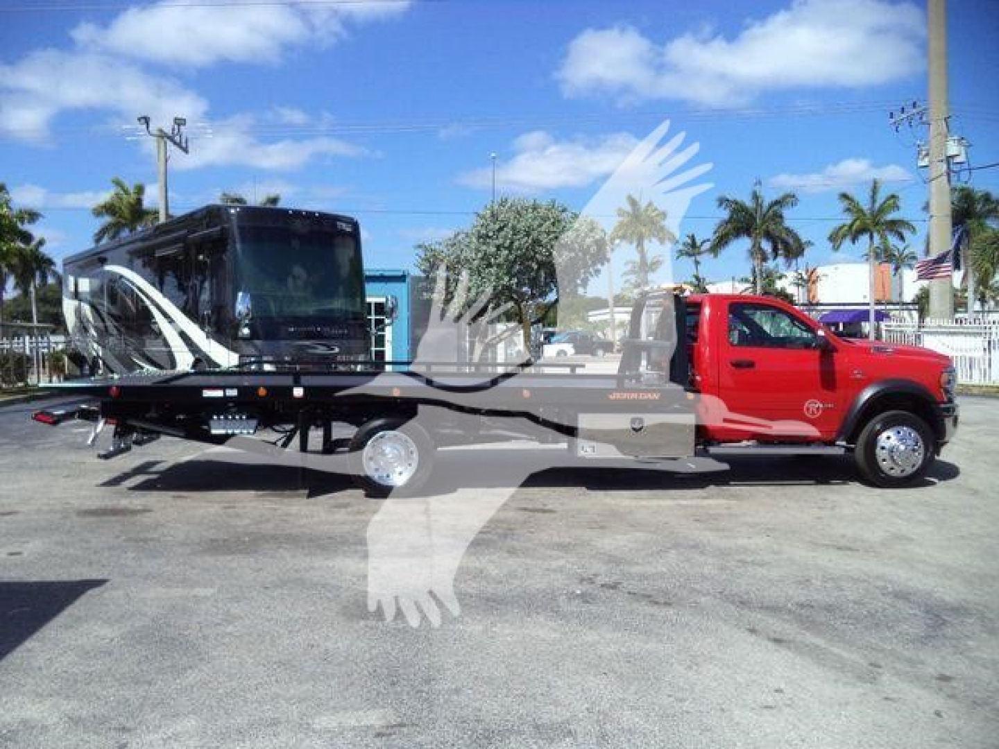 Tow truck with red cab and black rollback bed, side view showing hydraulic equipment and long flatbed.
