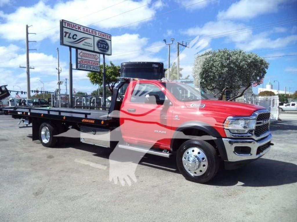Red Ram 5500 rollback tow truck in a dealership lot with a flatbed and company signage in the background.