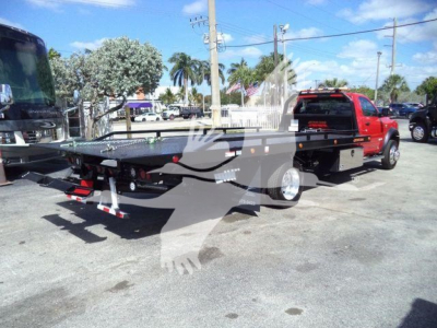 Flatbed rollback truck setup on a 2024 Ram 5500 SLT with dual rear wheels and a black steel flatbed, rear view showing hitch and LED taillights.