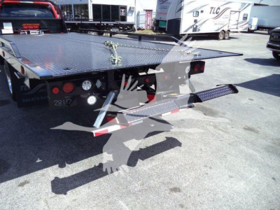Ram 5500 rollback tow bed showing dual rear wheels and diamond plate flatbed with under-platform controls and storage; metal steps and rear bumper visible.