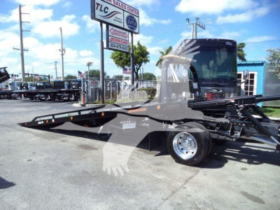 Tow truck rollback bed mounted on Ram 5500 SLT chassis with hydraulic tilt/slide bed and black cab in dealership lot.