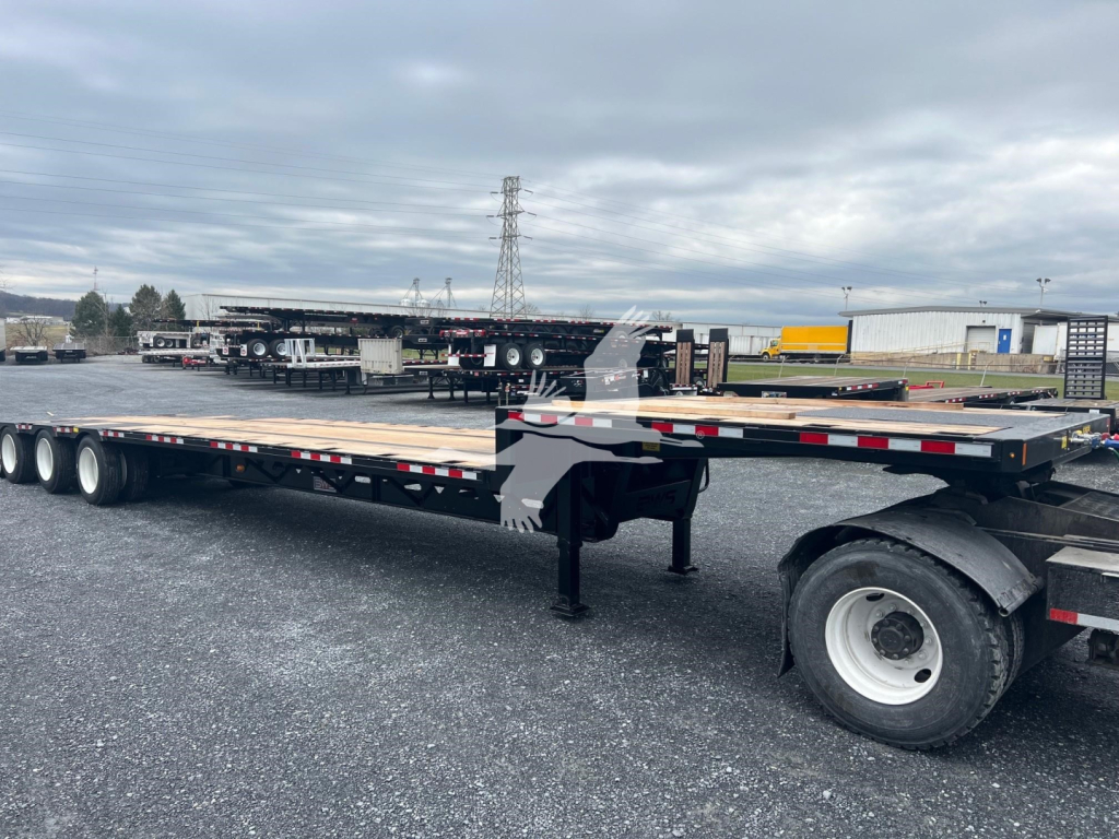 Trailer deck showing a drop deck middle-lift and multiple axles with black frame, white wheels, and surrounding lot.