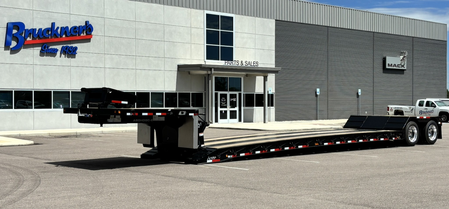 Lowboy trailer in front of sales building showing long hyd detach double drop extendable flatbed with extendable deck and dual rear axles.