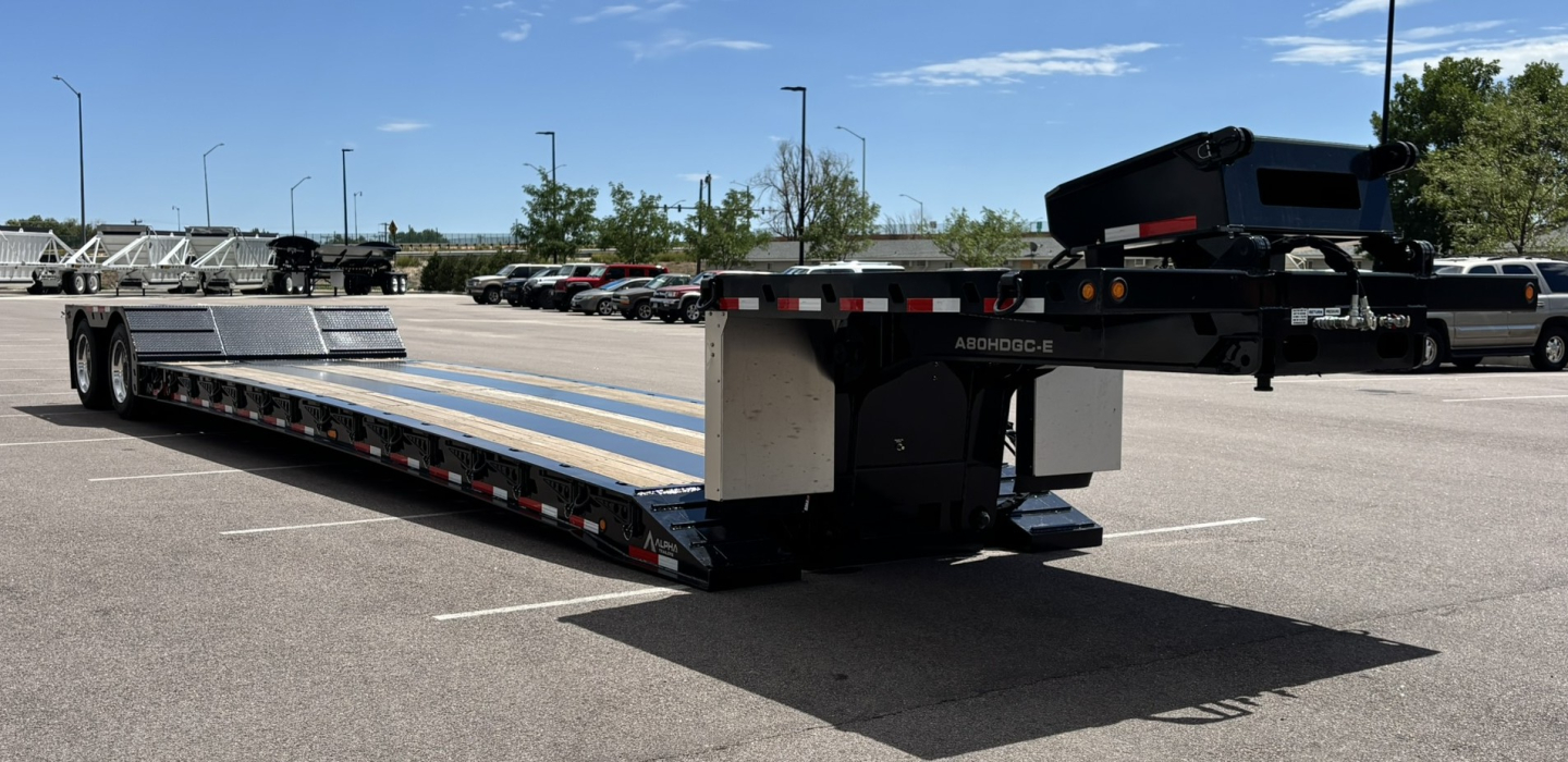 HDGC-E 48-foot lowboy trailer with hydraulic detachable double drop extendable ramps, viewed in parking lot with long flatbed and rear chassis tag.