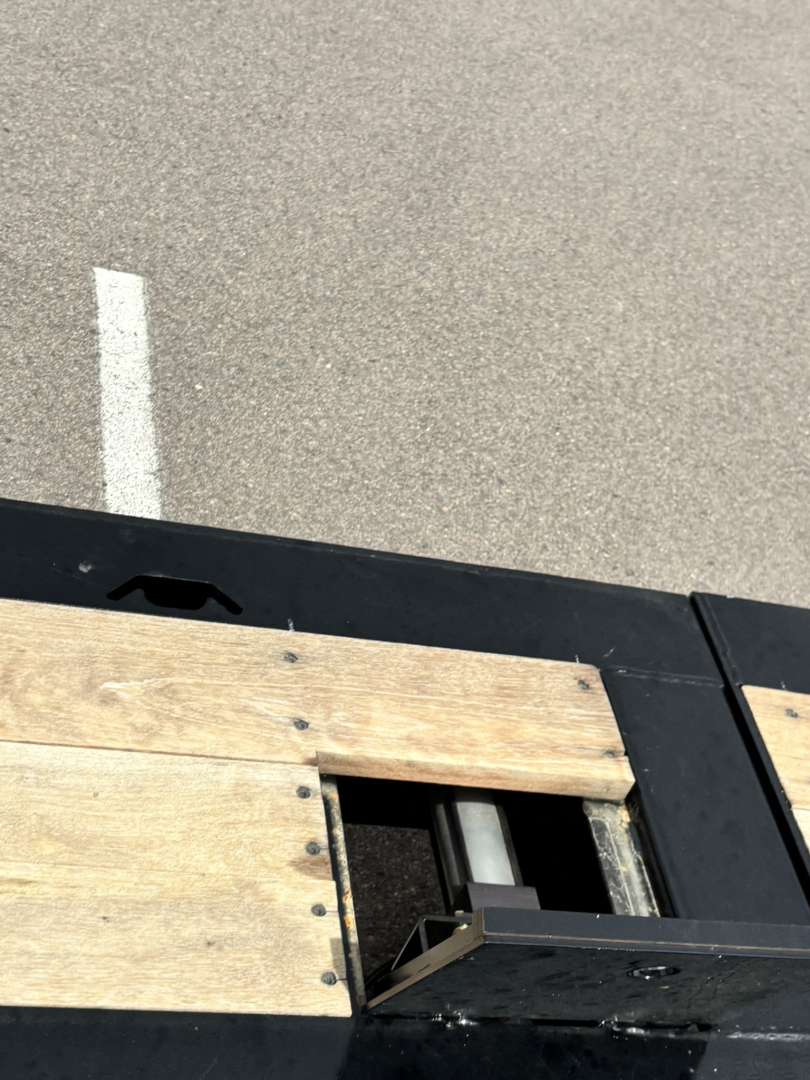 Lowboy trailer deck with wooden boards and metal frame, cutout area for hydraulic components visible.