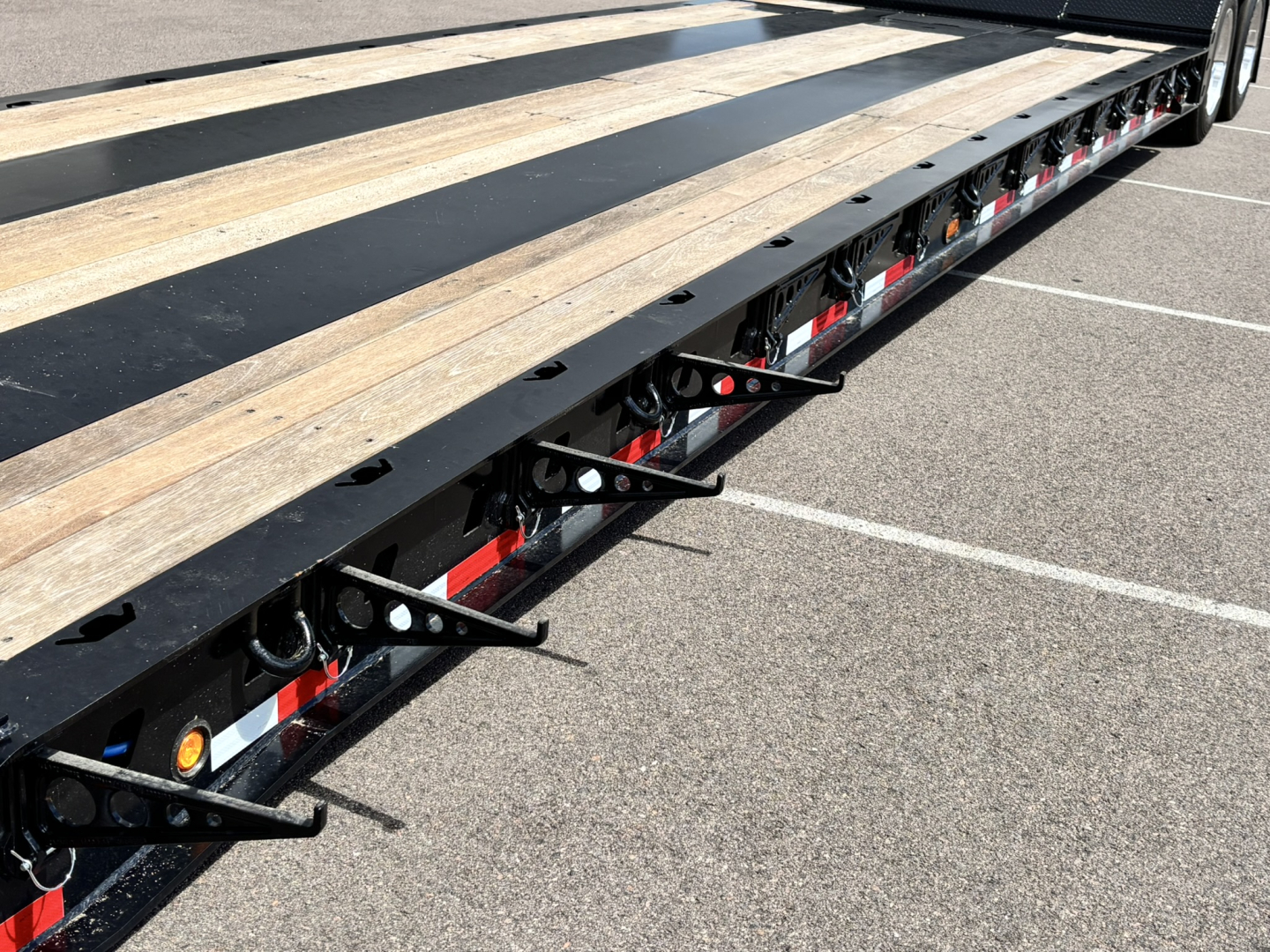 Trailer side rail showing wooden deck planks and black steel frame with red and white reflective tape along the edge.