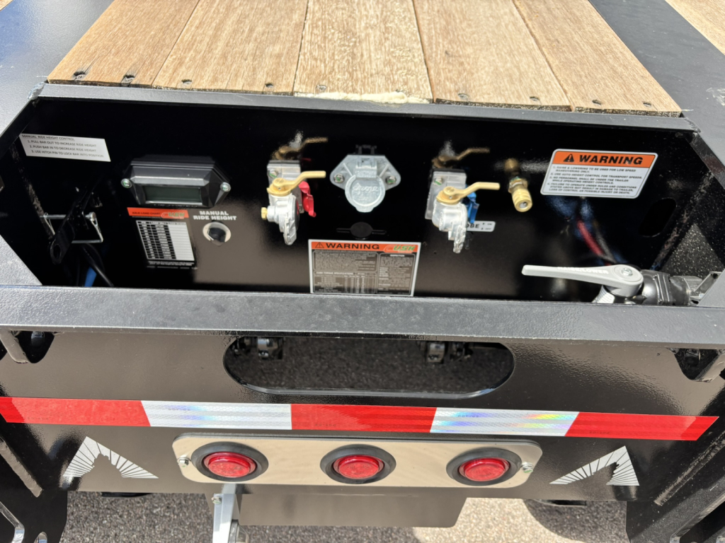 Trailer rear view showing control panel with warning labels, gauges, and hydraulic components on a wood deck—HDGC-E 48' lowboy trailer.