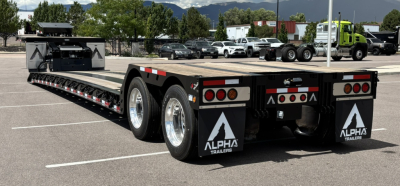 Lowboy trailer with extendable hyd detachable double drop; Alpha Trailers logo on mudflaps; dual rear axle; long flatbed with bed rails; multiple tail lights and reflectors.