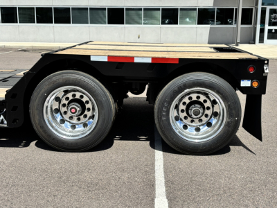 Trailer side view showing dual axles and wood deck, black frame, chrome wheels, reflective tape, and small rear fender area.