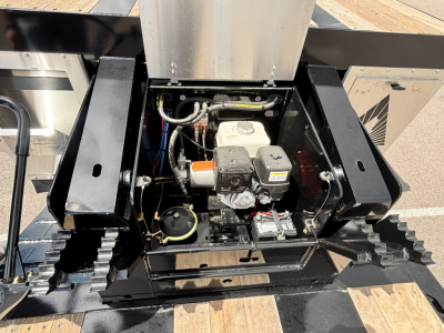 Engine bay of 2027 Alpha A80 HDGC-E trailer showing compact hydraulic unit with battery, hoses, and control box. Visible labels include small white reservoir cap and black hydraulic components.
