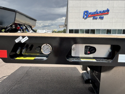 Lowboy trailer rear with pressure gauge and control panel, labels, and hydraulic components visible.
