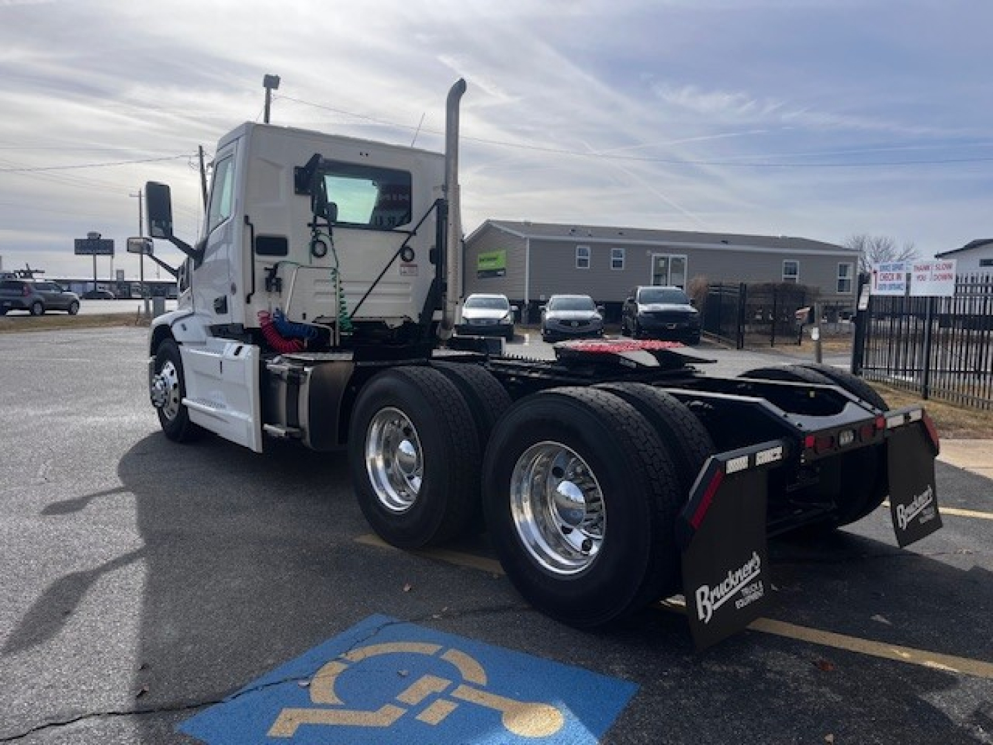 White 2026 Mack PR64T conventional day cab tractor seen from rear-side, dual rear axles, chrome wheels, with black RamAir mud flaps and fuel lines visible; cab interior not visible.