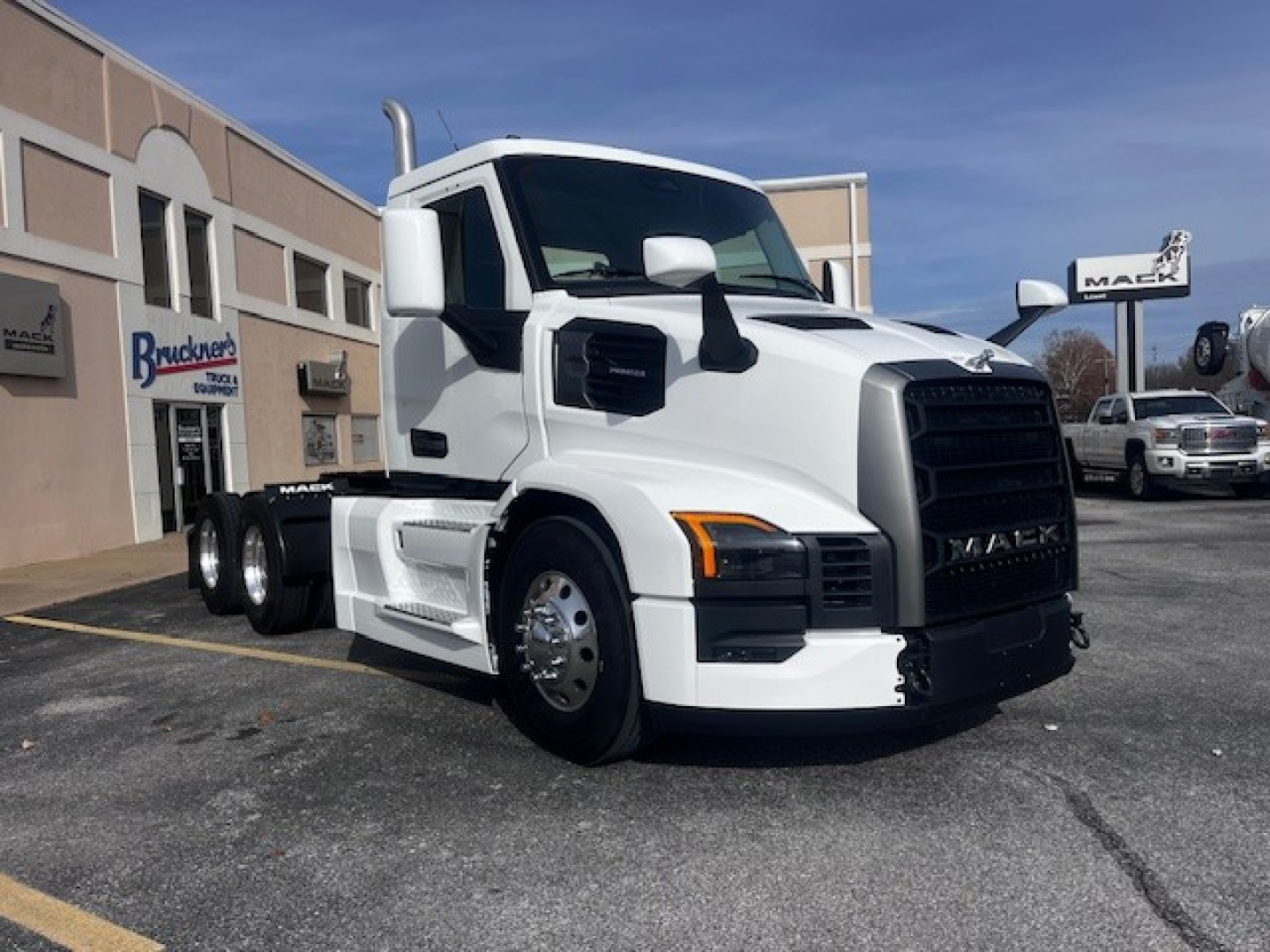 Truck cab exterior showing 2026 Mack PR64T with white paint, black grille, large side mirrors, and dual rear axles in a dealership lot.